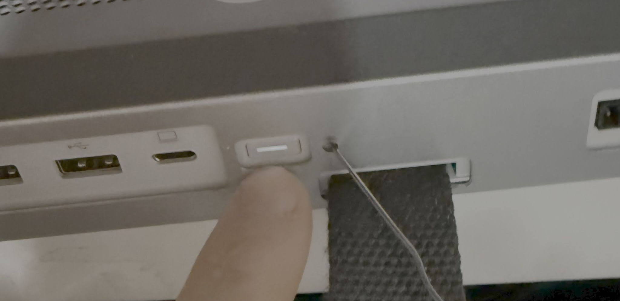 Finger pointing to reset button, with paperclip in the reset hole